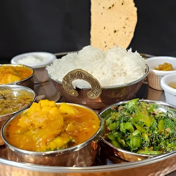 Indian thali with rice, curries, and papadum served in metal bowls on a tray.