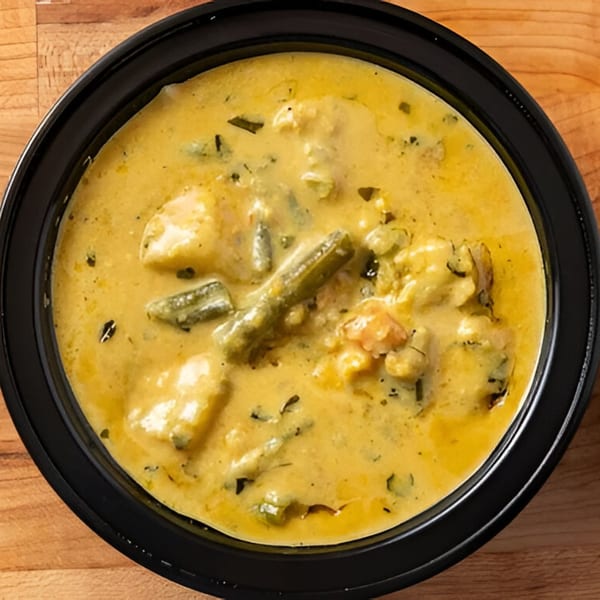 A close-up overhead view of a creamy yellow Indian curry with vegetables in a black bowl.